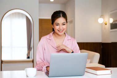 Genç neşeli, mutlu, pozitif, güzel, iş kadını ofiste dizüstü bilgisayar kullanarak oturuyor.