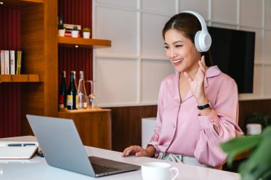 Gülümseyen Asyalı kadın, kulaklık takarak bilgisayar aracılığıyla müşteriyle iletişim kuruyor..
