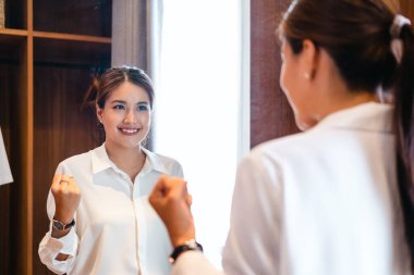 Genç, güzel Asyalı kadın aynanın önünde mutlu bir şekilde giyinmiş. İyi görünüyor ve kendine güveni tam..