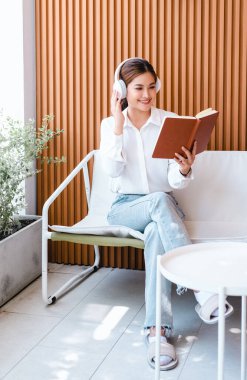 Güzel Asyalı yetişkin kadın kitap okuyor ve terasta açık havada müzik dinliyor. Yaşam tarzı ve insanların evdeki hayattan zevk alma konsepti