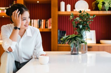 Elinde kahve fincanı tutan gülümseyen kadın başka tarafa bakıyor. Genç bir kadın mutfağında çay ya da kahve içerken işe gitmeye hazırlanıyor..