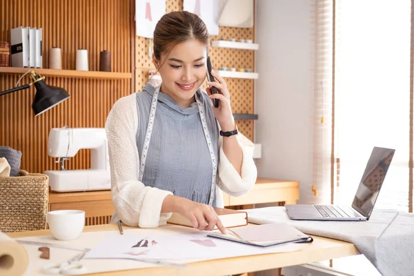 Terzilik Şirketi Konsepti Bespoke Moda Kıyafeti. Asyalı Bayan Tasarımcı Konuşuyor, Telefonla Müşteri Danışmanı. İş kadını Not Yazıyor, Modern Yaratıcı Dressmaking Stüdyosunda Çizim Yapıyor