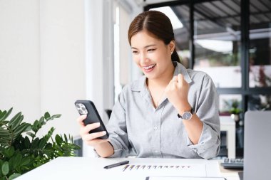 Asyalı kız bunu cep telefonu ve dizüstü bilgisayarla kutluyor, başarı pozu veriyor. E-ticaret, üniversite eğitimi, internet teknolojisi ya da küçük işletme konsepti. Kopyalama alanı olan modern ofis