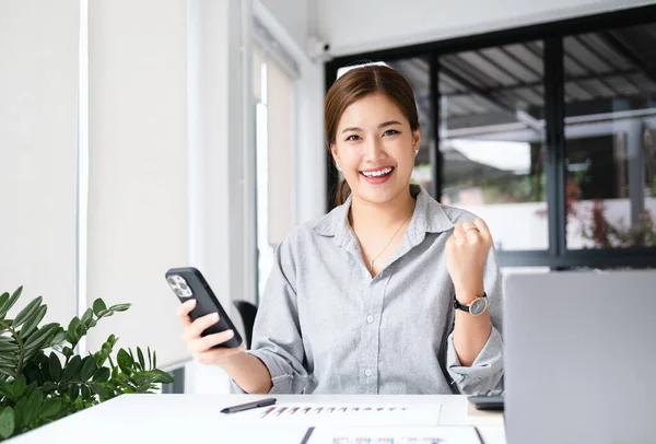 Asian girl celebrate with mobile phone and laptop, success happy pose. E-commerce, university education, internet technology, or startup small business concept. Modern office  with copy space