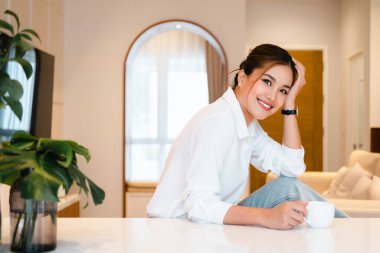 Neşeli genç bayan evde bir fincan kahvenin tadını çıkarıyor. Gülümseyen güzel kız, sabah sıcak çay içiyor.