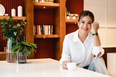 Genç ve mutlu bir kadın sabahları mutfakta kahve içiyor..