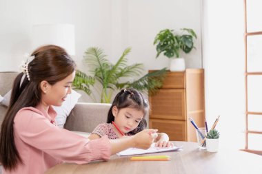 Mutlu aile annesi ve kızı birlikte resim yapıyorlar. Kadın kıza yardım ediyor. Genç Asyalı güzel anne ve kızı evde resim yapıyor..
