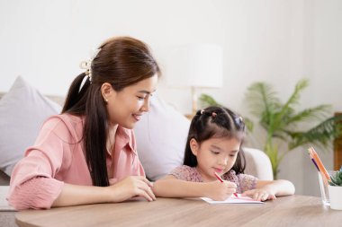 Mutlu aile annesi ve kızı birlikte resim yapıyorlar. Kadın kıza yardım ediyor. Genç Asyalı güzel anne ve kızı evde resim yapıyor..