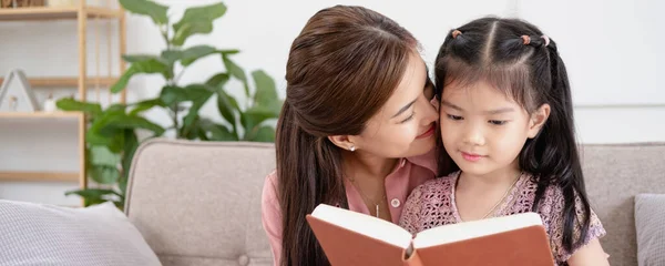 Sevgi dolu genç bir anne, tapılası küçük kızına kitap okuyor oturma odasında rahat bir koltukta oturuyor, anne anaokulu kızına öğretmenlik yapıyor, aile hafta sonunu evde birlikte geçiriyor, çocuk eğitimi veriyor.