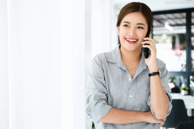 Modern ofiste çalışan Asyalı iş kadını bir telefon görüşmesi yapıyor ve gülümsüyor. .