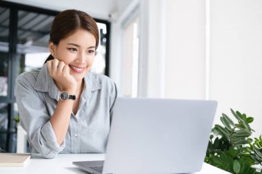 Ofiste dizüstü bilgisayarda çalışan neşeli iş kadını iş yerinde gömlek giyen Asyalı mutlu iş kadını. Çekici bayan ofis çalışanı gülümsemesi.