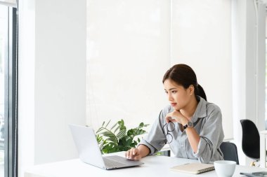 Gözlüklü Asyalı kadın masamda oturup dizüstü bilgisayara bakıyor, ödevini yapıyor, çalışıyor gibi görünüyor, arama çözümü ya da fikirler. İş mücadelesi, görev üzerinde düşünme kavramı