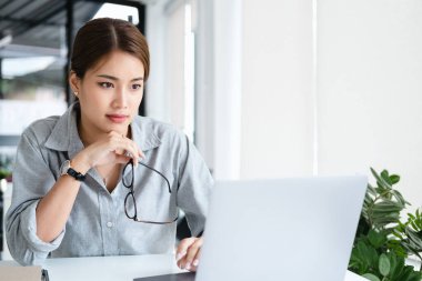 Düşünceli ve odaklanmış genç Asyalı kadın dizüstü bilgisayarına bakıyor, evdeki görevleri üzerinde çalışıyor. ev kavramından çalışma