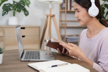 Evde çalışan genç bir kız öğrenci. Bilgisayarı kullanıyor ve internetten öğreniyor. İnternette web sitesi izleyen çekici bir kız öğrenci kulaklık takan, müzik dersi dinleyen, e-öğrenim eğitimi alan bir kadın..