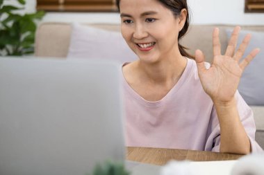 Pozitif neşeli Asyalı kızın yakın plan fotoğrafı çevrimiçi video çağrısı yayını yapıyor blogcularla görüşüyor merhaba dalgası el oturma masası ev içinde dizüstü bilgisayar kullanıyor.