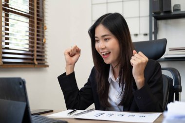 Online Asyalı kadın indirimi. Satış başarısından memnun. Kollarını kaldırıp kutlama yapan başarılı bir iş kadını. Heyecanlı Asyalı kadın masada oturur ve online piyango kazanmaktan mutlu olur..