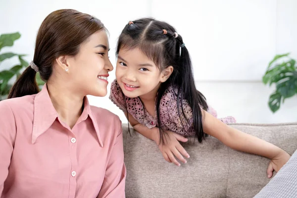Asian mother kissing her daughter in bright living room at home.
