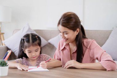 Eğitimsel hobi çocuk konseptinde yaratıcılık yeteneği geliştirir. Asyalı anne küçük kızı güneşli bir oturma odasında, anne kıza resim yapmayı öğretiyor kağıt ve renkli kalemler kullanıyor.