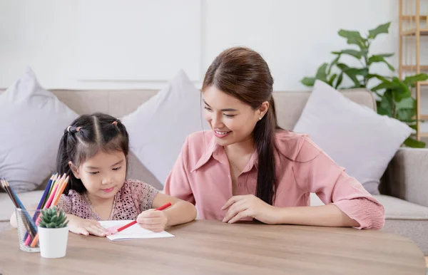 Happy asian young mother smile with daughter in living room at home. Asian young mother teaching small daughter to drawing reading and writing to develop her daughter skill. Home School Concept
