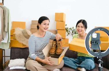 Moda mağazasında genç Asyalı kadın işyeri sahibi müşteriye moda kıyafetleri satmak için akıllı telefon canlı yayını yapıyor ve sosyal medya, çevrimiçi alışveriş konseptinde detaylar sunuyor..