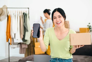 Moda tarzındaki güzel Asyalı kadınlar izole edilmiş arka planda bir sürü paket kutusu ve cep telefonu ödeme uygulaması tutuyorlar. Çekici yeşil tişörtlü mutlu kadın alışverişe gidiyor.