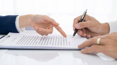 Avukat, erkek müşteriye toplantıda imzalı satış sözleşmesi yazacağı yeri gösteren sigorta sözleşmesine işaret ediyor. Finansal iş anlaşması, banka kredisi hizmeti, yakın görüş.