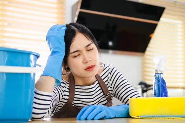 tired woman cleaner in apron and gloves for cleaning sitting with bucket for cleaning on kitchen background, sad girl housewife cleans on house background, cleaning service worker