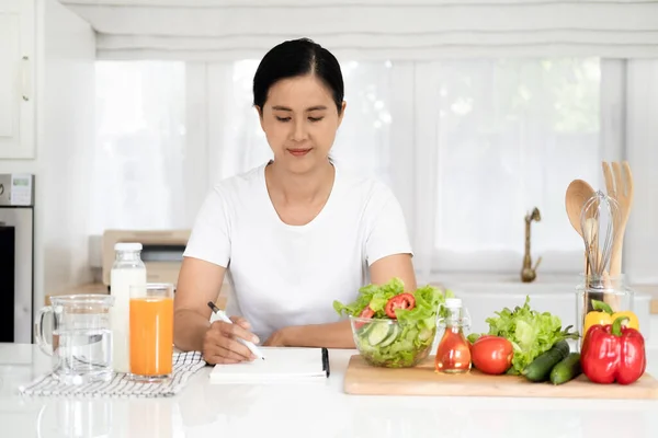 Diet, Dieting asian woman write diet plan right nutrition on table with fresh vegetables salad,  is different food ingredients in the green. Nutritionist of healthy, nutrition of weight loss.