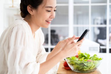 Mutfakta yemek pişirirken cep telefonu kullanan gülümseyen genç bir kadın masaya yaslanan neşeli bir kadın cep telefonundan mesajlar okuyan ve gülümseyen, bedava fotokopi çeken bir kadın.