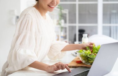 Mutfakta bilgisayarla ellerinizi kapatın. İnternetten yemek yapmayı öğrenin. Genç bir kadın mutfakta yemek pişirme dersi videosu seyrediyor. Dijital Tablet Tarifi 'nden sonra salata yaparken yemek tarifi okuyor..