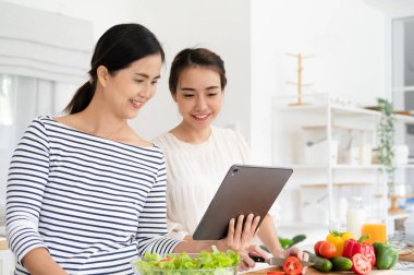 Asyalı kadınlar yemek pişirmek için malzemeleri tablet vasıtasıyla internet üzerinden aşçılık kursunda hazırlıyorlar. Modern yaşam tarzı kavramı için internet teknolojisi üzerine yemek içeriği