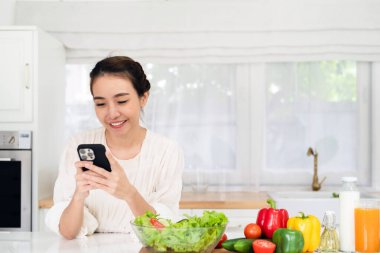 Mutfakta yemek pişirirken cep telefonu kullanan gülümseyen genç bir kadın masaya yaslanan neşeli bir kadın cep telefonundan mesajlar okuyan ve gülümseyen, bedava fotokopi çeken bir kadın.