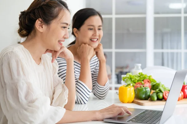 Asyalı kadınlar yemek pişirmek için malzemeleri tablet vasıtasıyla internet üzerinden aşçılık kursunda hazırlıyorlar. Modern yaşam tarzı kavramı için internet teknolojisi üzerine yemek içeriği