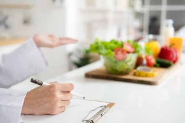 Diyetisyen el yazısını kapat ve arka planda farklı sağlıklı besin maddeleri olan bir diyet planı üzerinde çalış. Kilo kaybı ve doğru beslenme konsepti