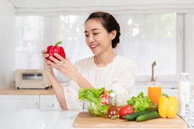 Mutlu Asyalı kadın sağlıklı vejetaryen yemekleri pişirmeye hevesli ve elinde iştah açıcı bir dolma biber tutuyor..