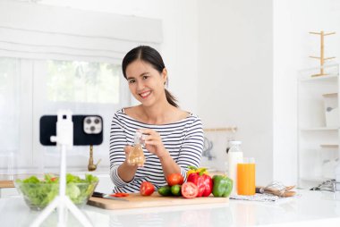Genç kadın video blogcusu mutfakta salata pişiriyor ve film çekiyor.