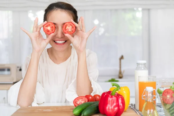 Young fun vegeterian housewife woman in casual clothes cover eye with tomato cooking food in light kitchen at home alone Healthy diet lifestyle concept.