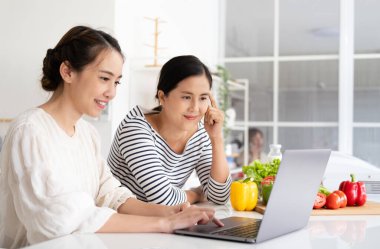 Asyalı kadınlar taze sebze pişiriyor salata malzemelerini karıştırıyor lezzetli vejetaryen yemekleri pişiriyor çevrimiçi blogcu tarifi defterini içeride arıyor.