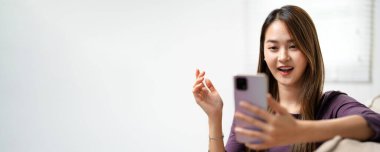 Evde akıllı telefon cihazıyla cep telefonu tutan mutlu Asyalı genç kız. Gülümseyen Asyalı genç kadın blogcu yeni sosyal medya aboneliği, internetten satın alma, uygulamalardan ürünler sipariş etme.