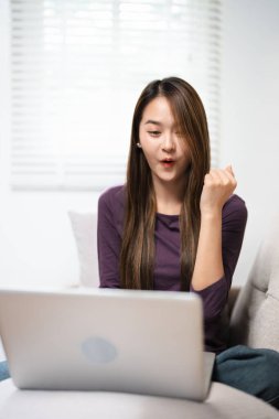 Heyecanlı bir kadın dizüstü bilgisayar ekranına bakıyor, iyi haberlere seviniyor, mutlu gülen kız e-posta ya da sosyal ağda mesaj okuyor, online ödül kazanıyor, harika bir alışveriş teklifi yapıyor, evdeki rahat koltukta oturuyor.