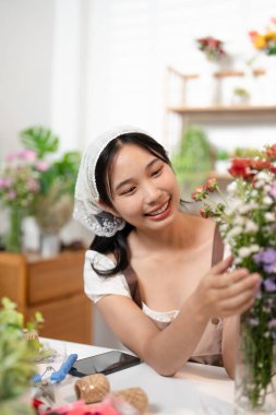 Önlüklü kadın çiçekçi gülümsüyor ve çiçekçide iş arkadaşıyla çiçek buketi düzenlemek için çiçek tasarlıyor. .