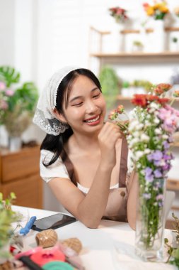 Çiçek vazosu yapan mutlu genç bayan. Çiçekçide çalışan çiçekçi. Çiçek buketi teslimatını ayarlamak için müşteri siparişinden liste hazırlayan genç Asyalı çiçekçi..