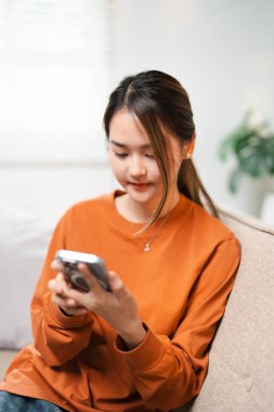 Evde akıllı telefon cihazıyla cep telefonu tutan mutlu Asyalı genç kız. Gülümseyen Asyalı genç kadın blogcu yeni sosyal medya aboneliği, internetten satın alma, uygulamalardan ürünler sipariş etme.