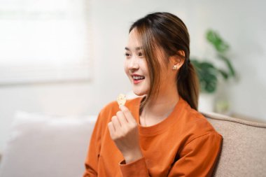 Rahat Asyalı kadın evde boş vakit geçiriyor, abur cubur yiyor ve televizyon izliyor. Heyecanlı gülümseyen bayan, oturma odasındaki kanepede dinlenirken sinemadan zevk alıyor.