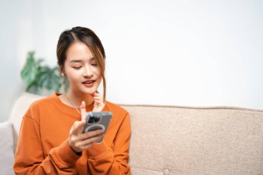 Evde akıllı telefon cihazıyla cep telefonu tutan mutlu Asyalı genç kız. Gülümseyen Asyalı genç kadın blogcu yeni sosyal medya aboneliği, internetten satın alma, uygulamalardan ürünler sipariş etme.