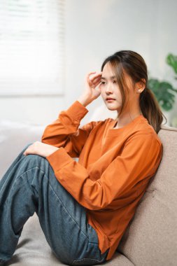 Alnına dokunan Asyalı kadın iş ya da ilişkiler yüzünden hayal kırıklığına uğramış, kanepeye oturmuş, dizlerini kucaklıyor, umutsuzluk ve endişe duyuyor, yalnızlık çekiyor, psikolojik sorunlar yaşıyor..