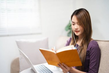 Dizüstü bilgisayarda oturan, kulaklık takan, oturma odasında oturan, işi birleştiren ve ders çalışan iş kadını..