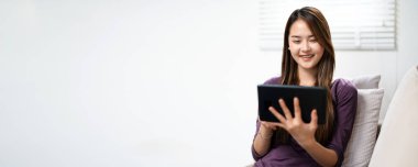 Modern bir bayan evde oturup, online bir kitap okumak için e-okuyucu tableti kullanıyor. Bir kadın evde yalnız başına teknoloji kullanarak kanepede dinlenmenin tadını çıkarıyor. Kapalı hayat