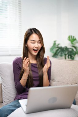 Heyecanlı bir kadın dizüstü bilgisayar ekranına bakıyor, iyi haberlere seviniyor, mutlu gülen kız e-posta ya da sosyal ağda mesaj okuyor, online ödül kazanıyor, harika bir alışveriş teklifi yapıyor, evdeki rahat koltukta oturuyor.