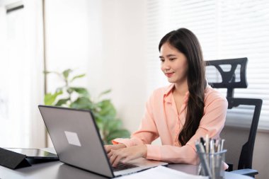 Modern işyerindeki bilgisayarında çalışan kendine güvenen iş kadını. Laptopla çalışırken gülümseyen Asyalı, mutlu ve çekici bir iş kadını..